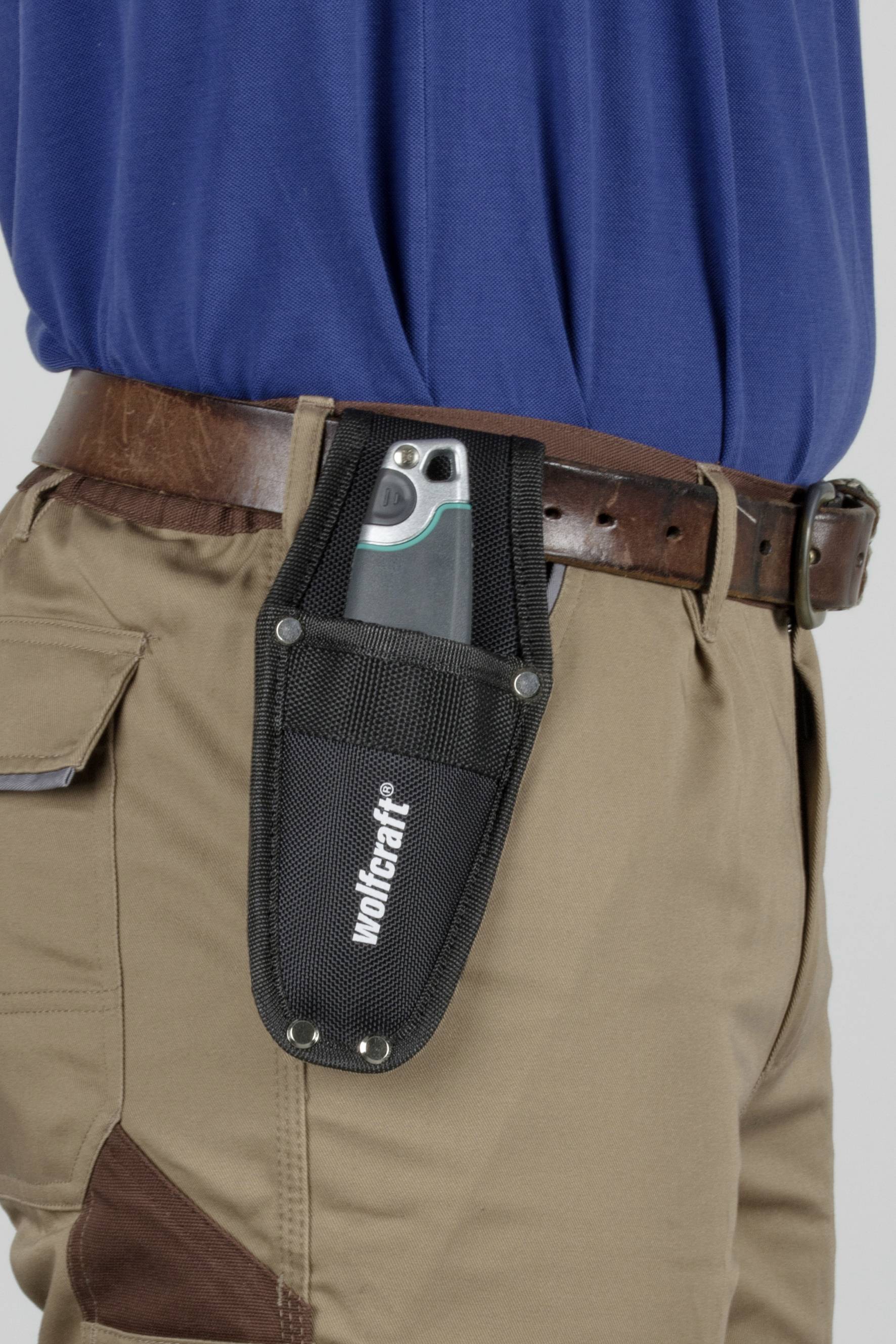 A person is wearing a multi-tool in a black belt pouch at the waist, dressed in a blue blouse and beige trousers.