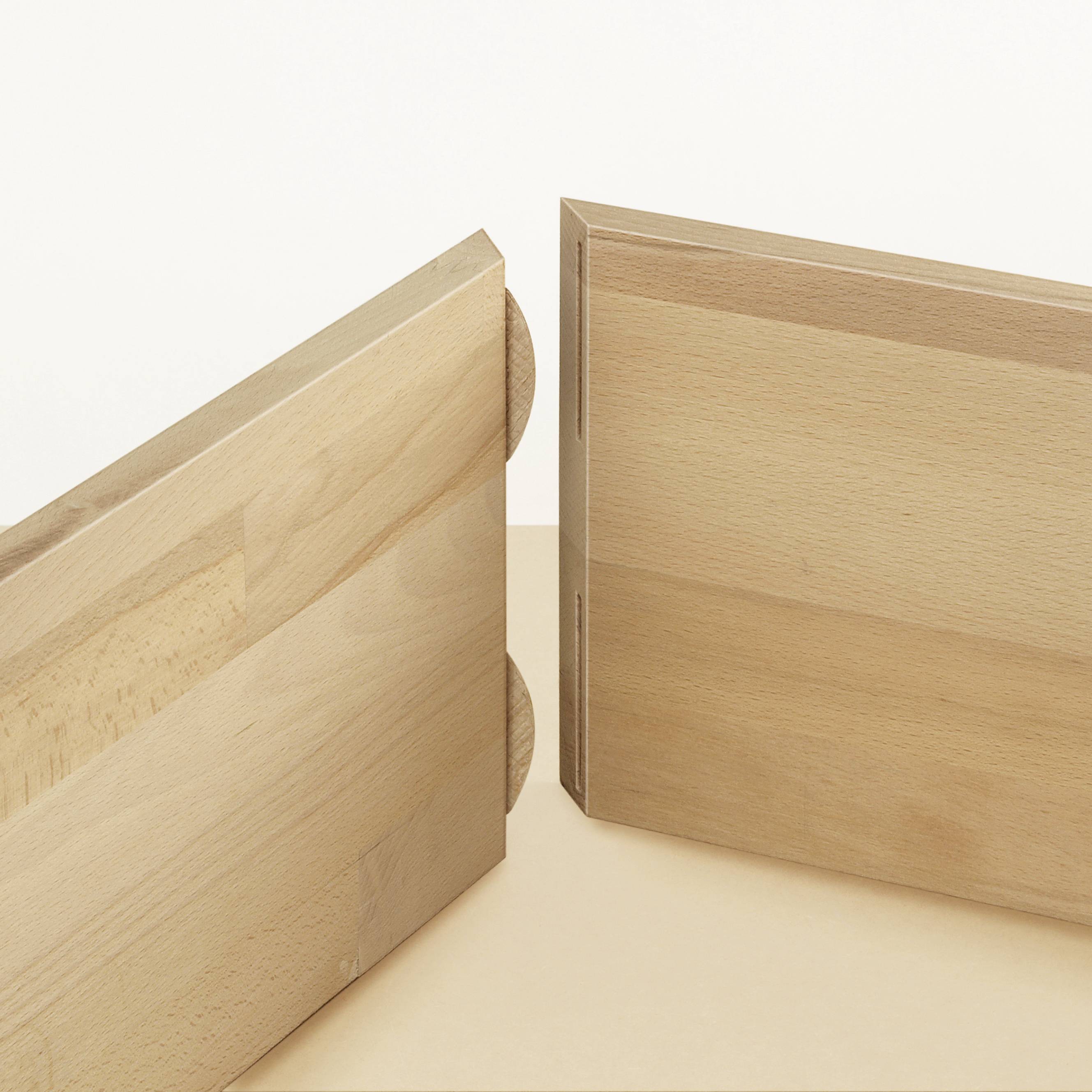 Two wooden planks in a light wood tone stand at right angles to each other on a light surface.