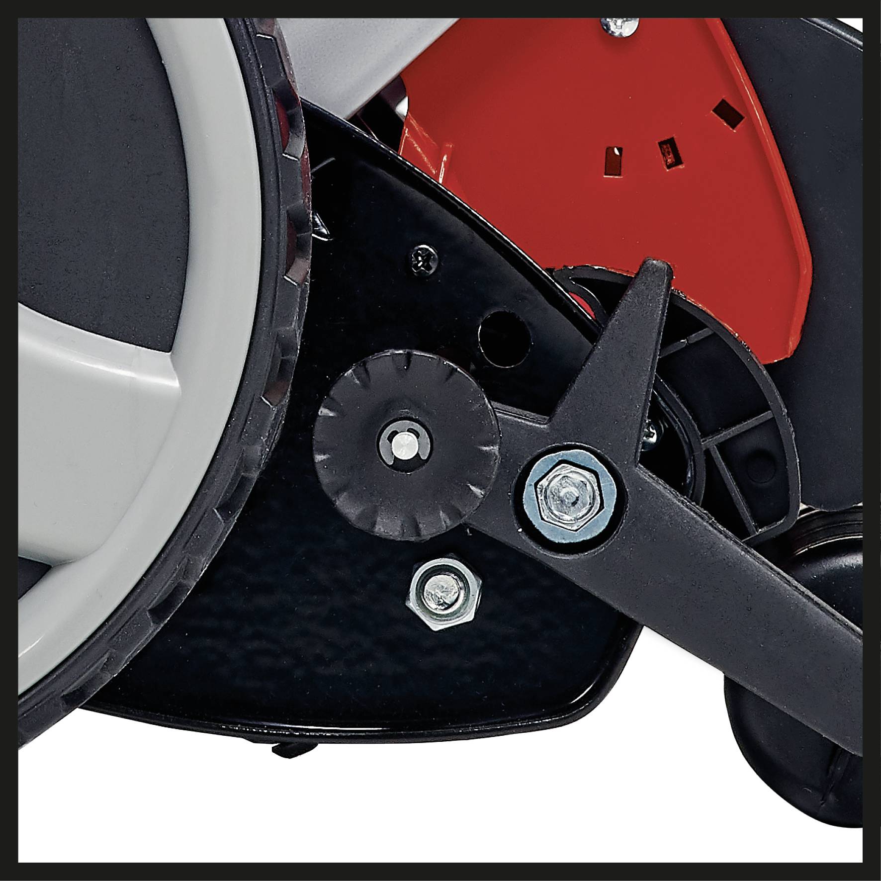 Close-up of part of a lawnmower. A wheel, fastening screws and a red casing component are visible.