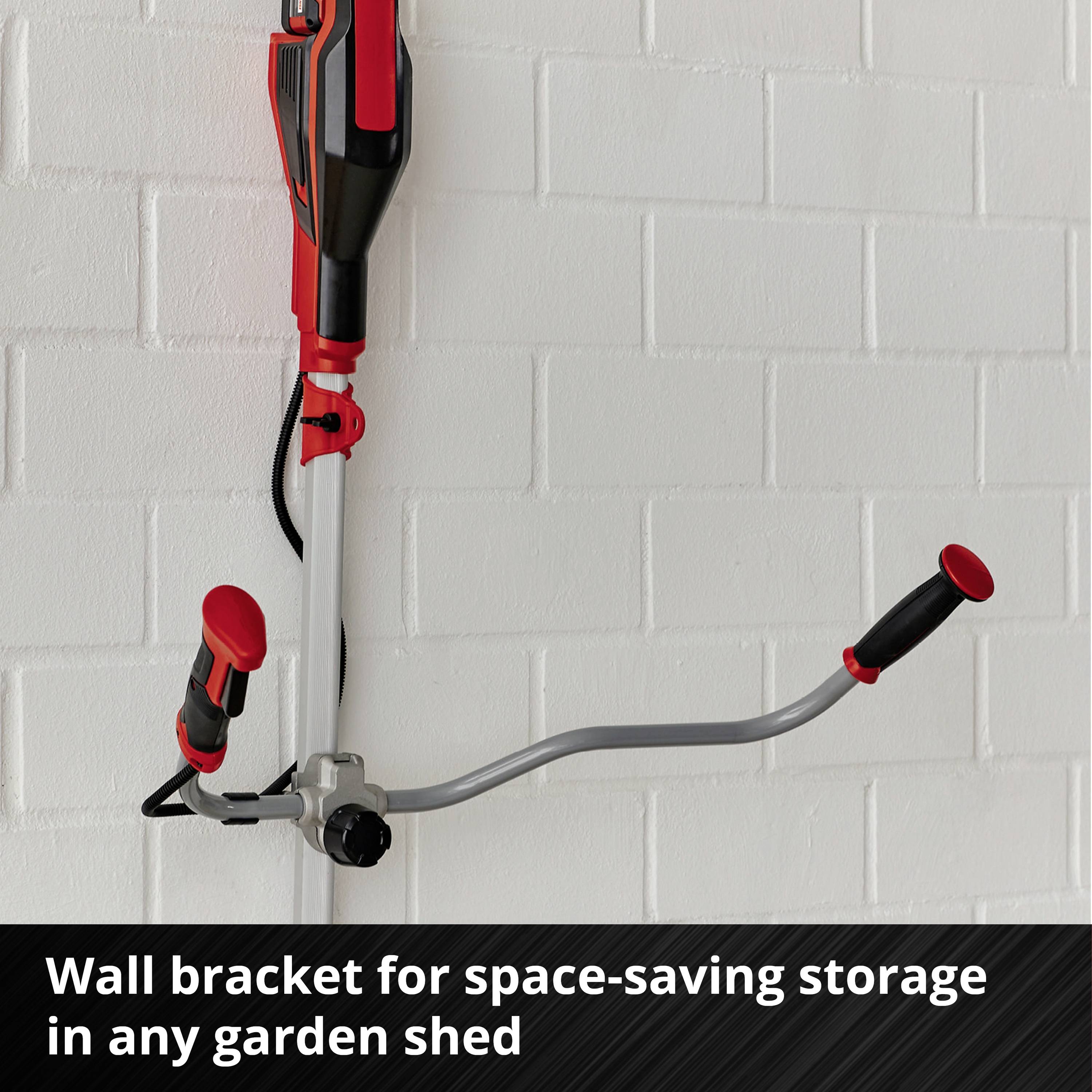 A red lawn trimmer hangs on a wall bracket in front of a white brick wall. Underneath it reads: 'Wall bracket for space-saving storage in any garden shed'.