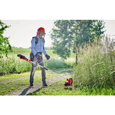 A person wearing protective equipment is using a strimmer to cut long grass beside a path in a rural setting.