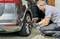 A man is kneeling beside a car and tightening the wheel nuts with an electric tool.