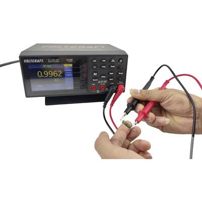 A person is measuring the resistance of a green resistor with a digital multimetre, which indicates 0.9962 kΩ.
