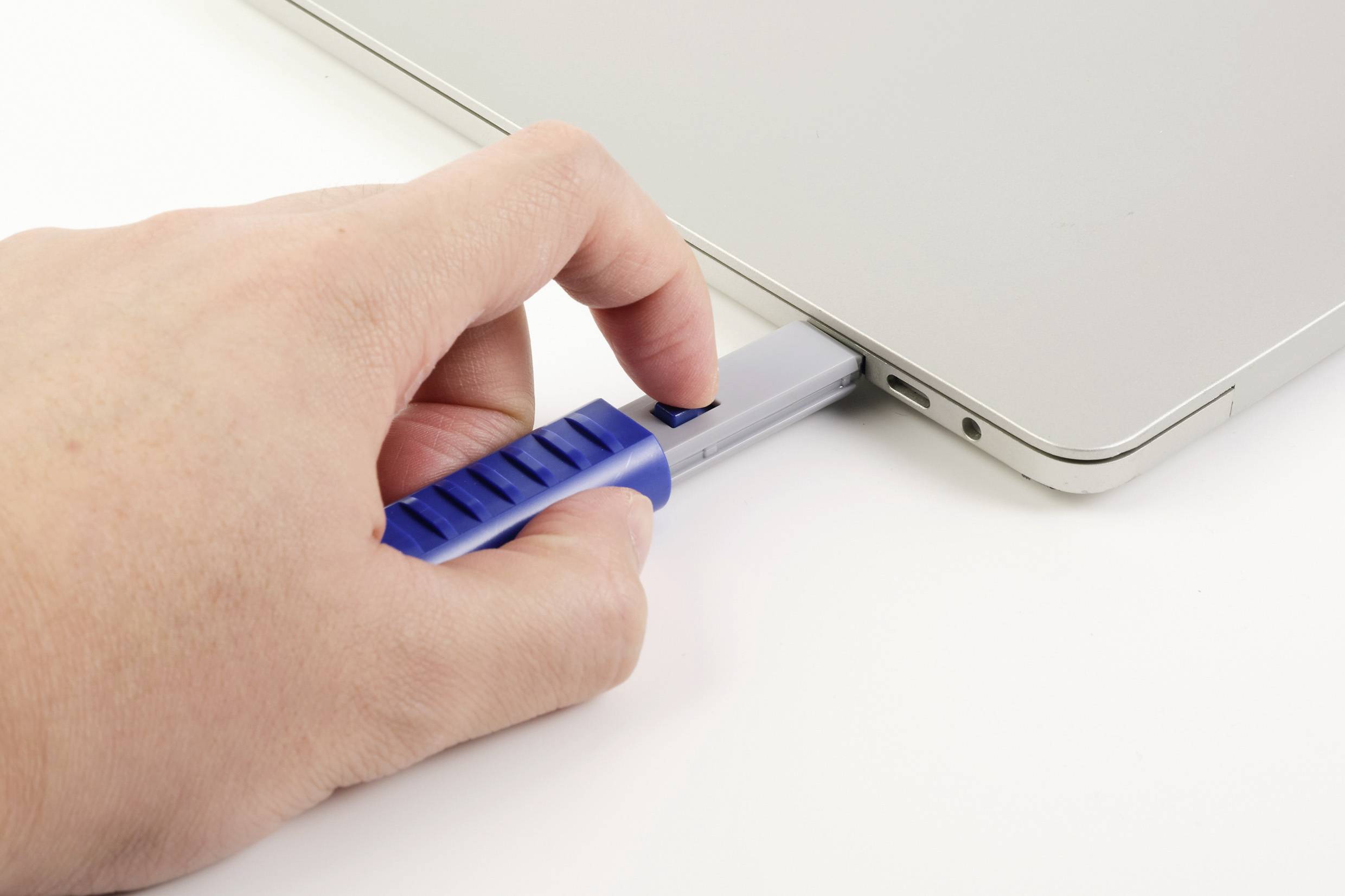 A hand is inserting a blue USB stick into a laptop port.
