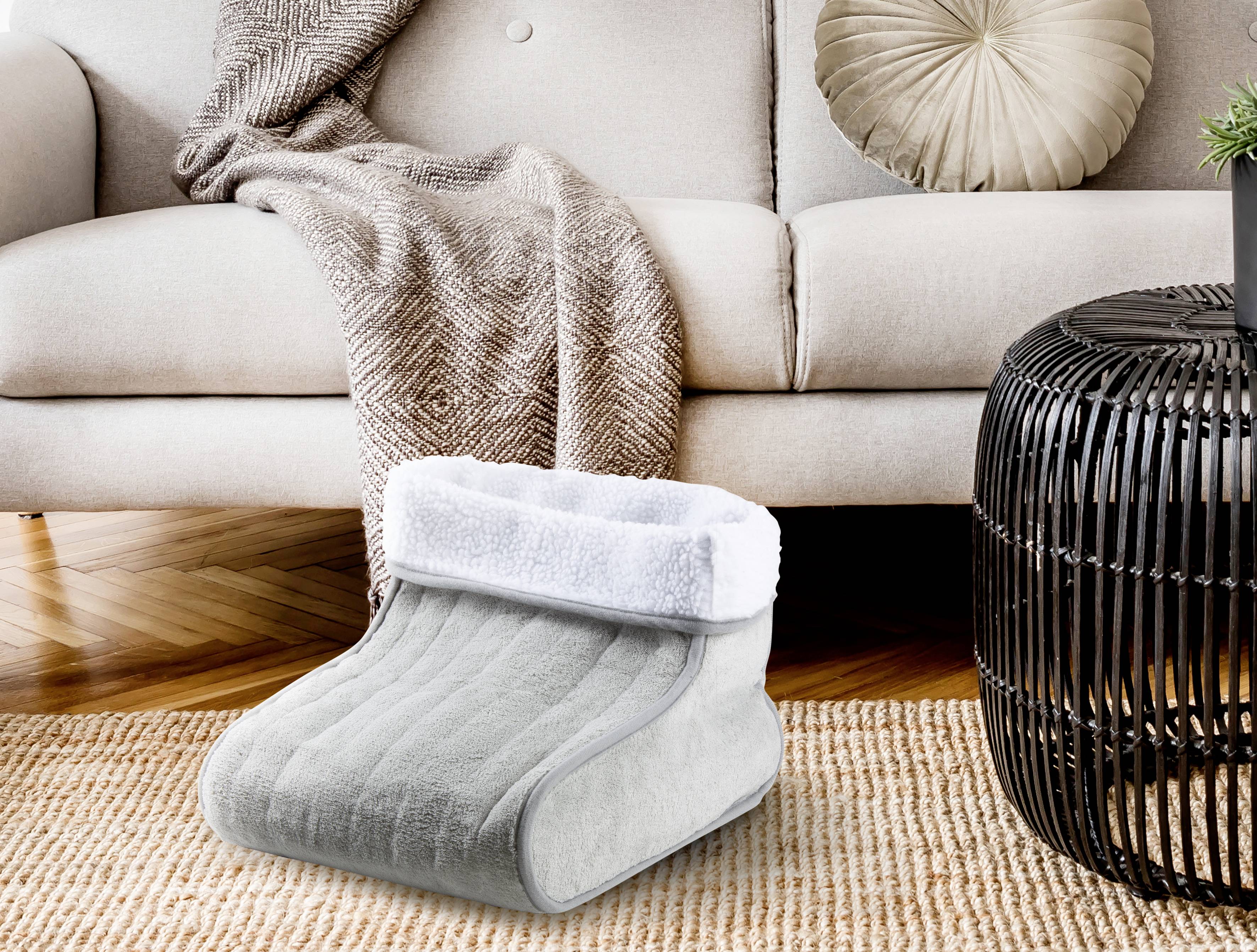 Grey foot warmer with soft lining placed in front of a cream-coloured sofa and footstool in a cosy living room.