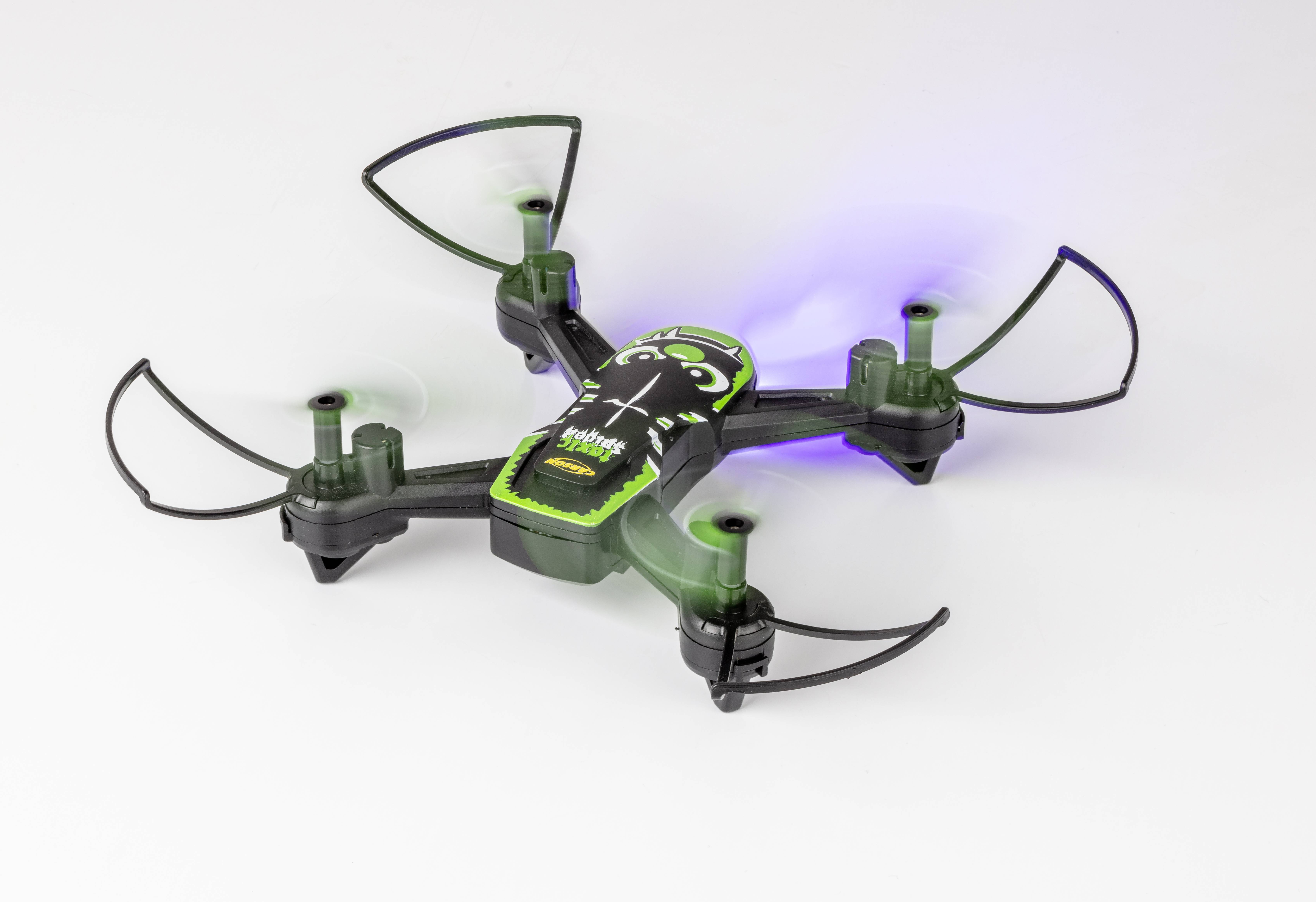 Small green drone with four rotors flies in a bright room. Lights on the rotor arms are partially switched on.