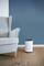 A white air humidifier stands on a wooden floor next to a light grey armchair in front of a blue wall.
