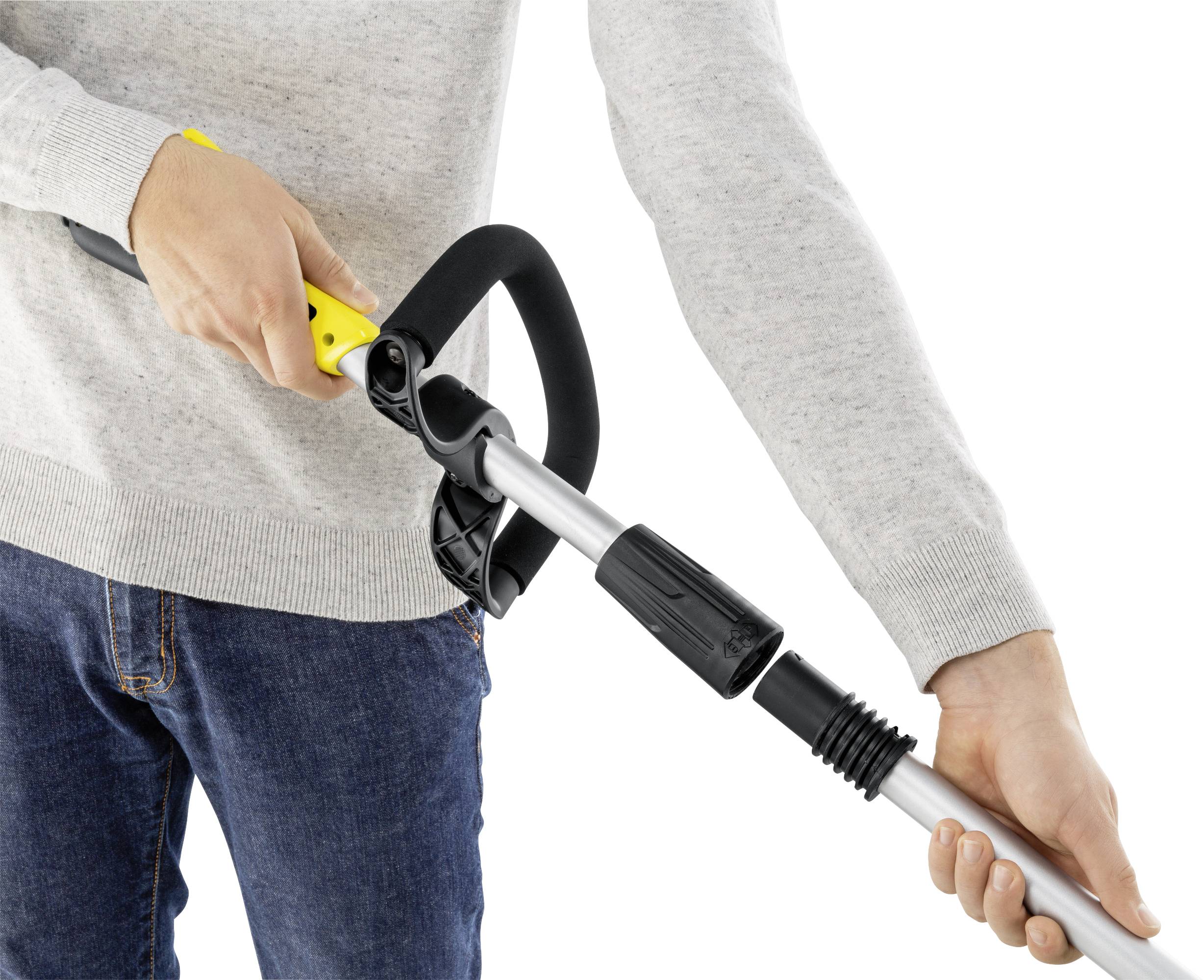 A person is attaching a telescopic handle to a cleaning device. Hands are gripping the yellow handle and the connection area firmly.