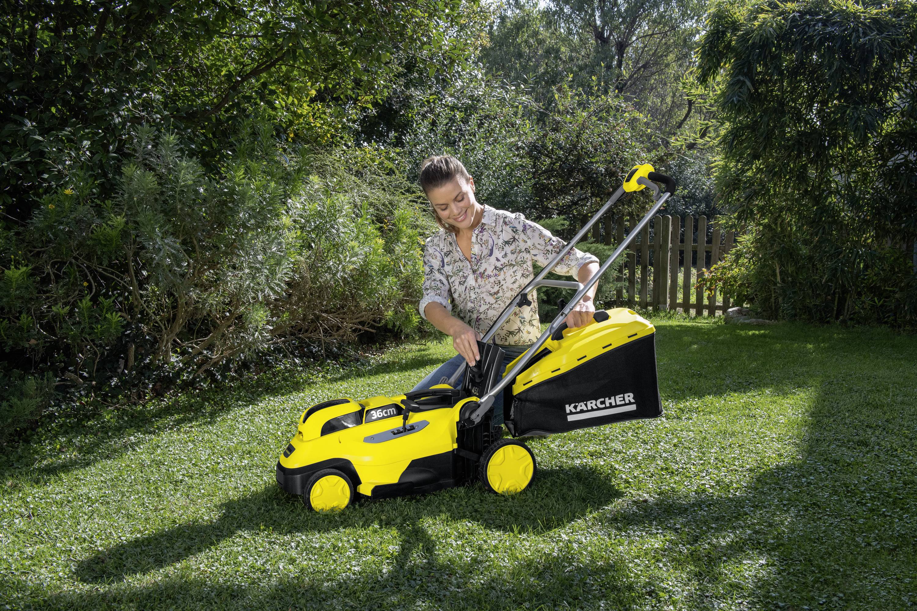 A person is mowing the lawn with a yellow lawnmower in a sunny garden.