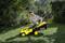 A person is mowing the lawn with a yellow lawnmower in a sunny garden.
