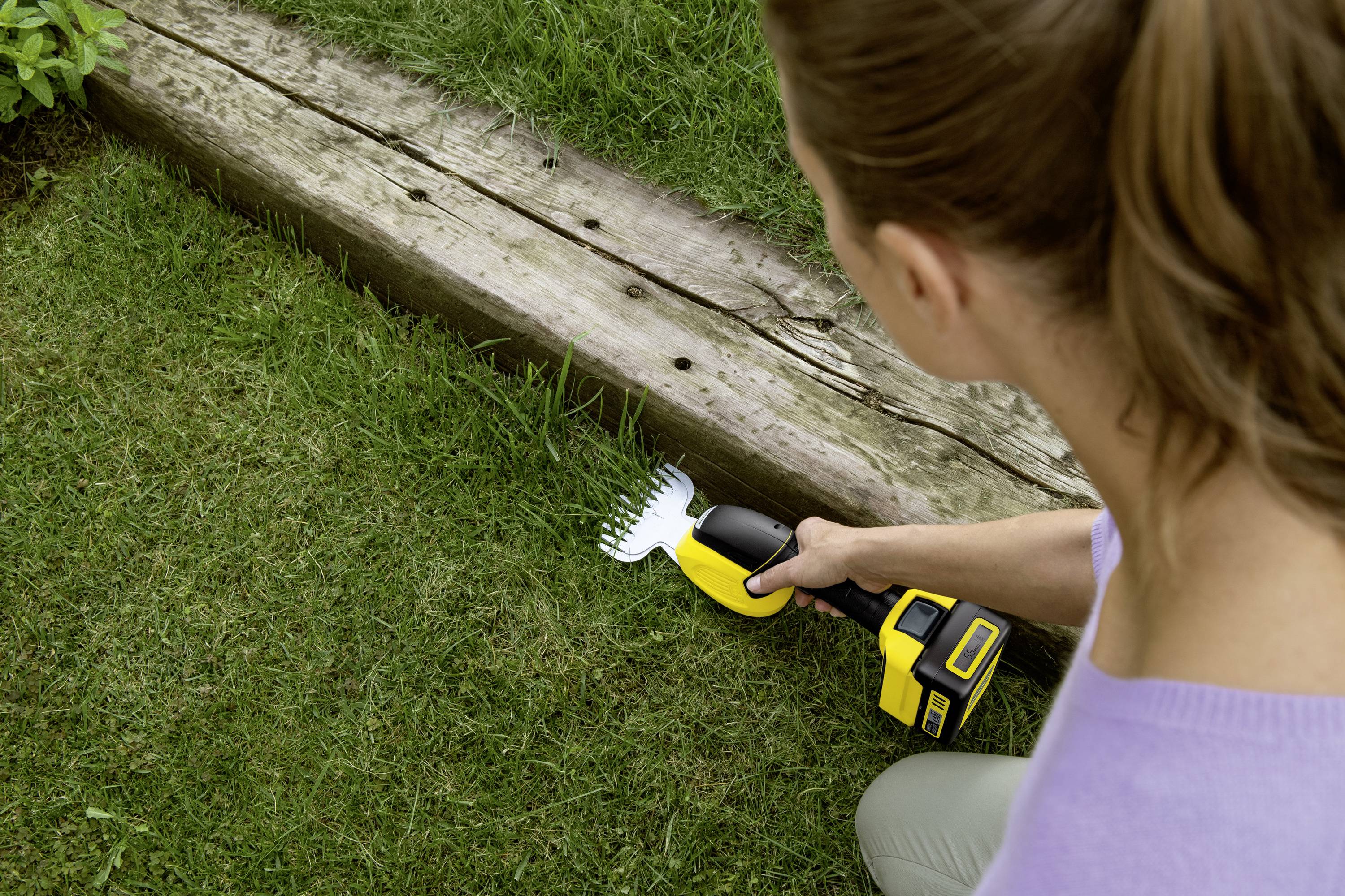 A person is trimming grass with an electric lawn trimmer along a wooden board on the lawn.