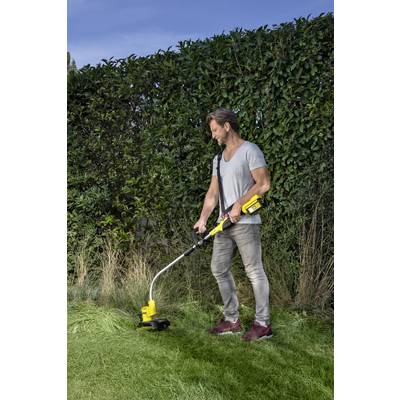 A person is mowing the lawn with a yellow lawn trimmer in front of a hedge on a sunny day.