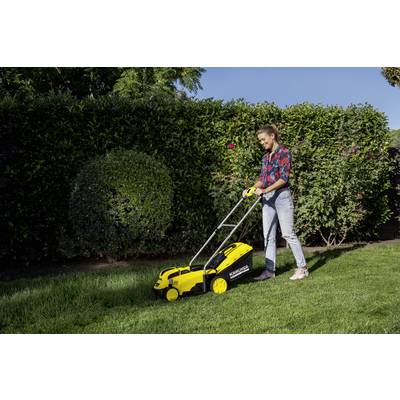 A person is mowing the grass-covered plot with a yellow lawnmower in front of a tall hedge on a sunny day.