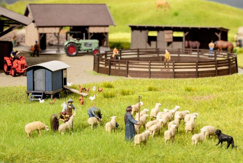 A miniature farm with figures herding sheep, surrounded by cottages, tractors and animals. A rural scene with people and animals in the foreground.