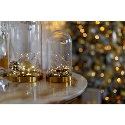 Glass bell jars with fairy lights on a table, with a blurred, illuminated Christmas tree in the background. Festive atmosphere and decoration.