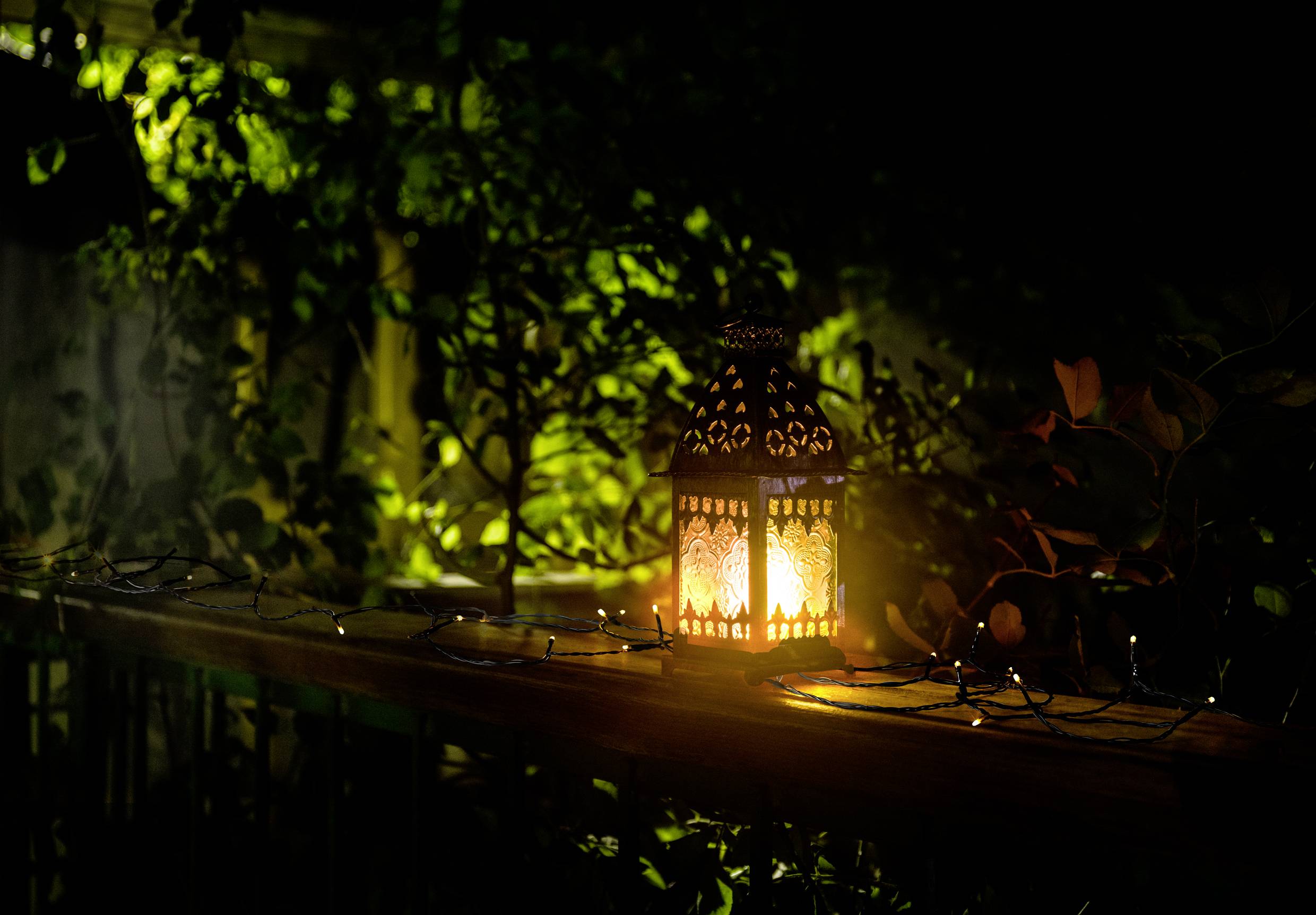 A decorative lantern sits on a wooden banister, radiating warm, yellow light. Leaves are visible in the background.