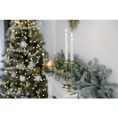 Candlesticks and pine branches on a mantelpiece, with a decorated Christmas tree adorned with lights in the background.