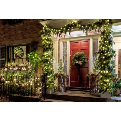 A festively decorated house entrance with red doors, framed by twinkling Christmas lights and wreaths. Welcoming atmosphere.