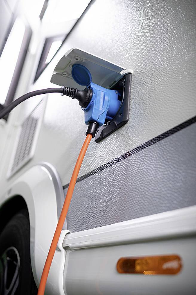 A campervan is powered via an orange cable. The charging point is located on the exterior of the vehicle.