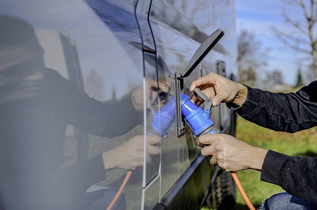 A person plugs a charging cable into the side of a vehicle outdoors to charge it.