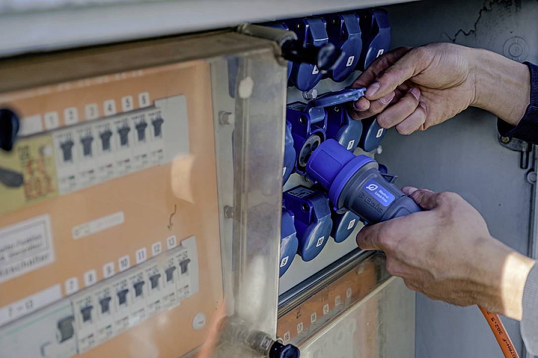 A person is connecting an electrical cable to a blue plug on a distribution board containing switches and fuses.