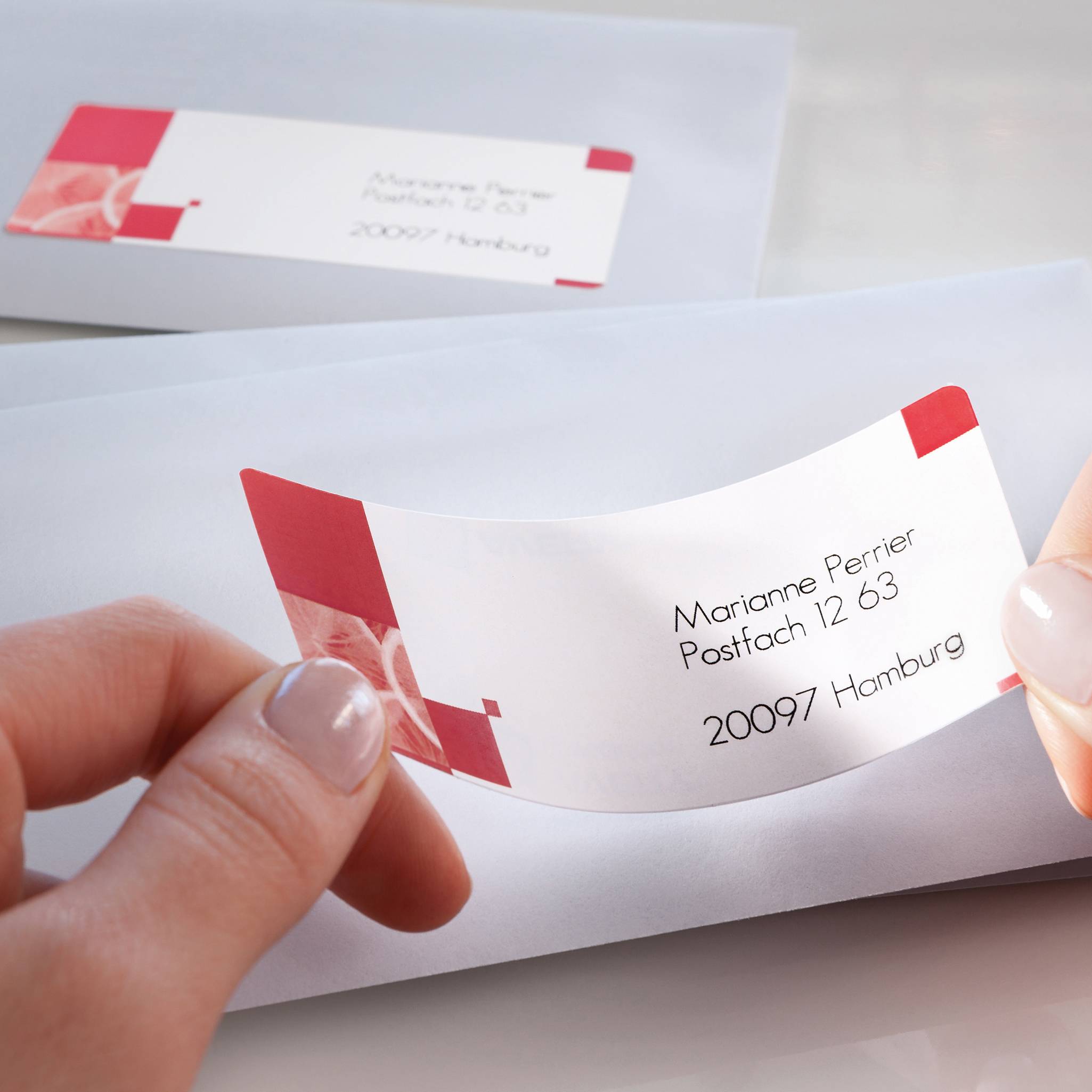 An envelope with a business card, which reads 'Marianne Perrier, PO Box 12 63, 20097 Hamburg'. Hands are holding the card.
