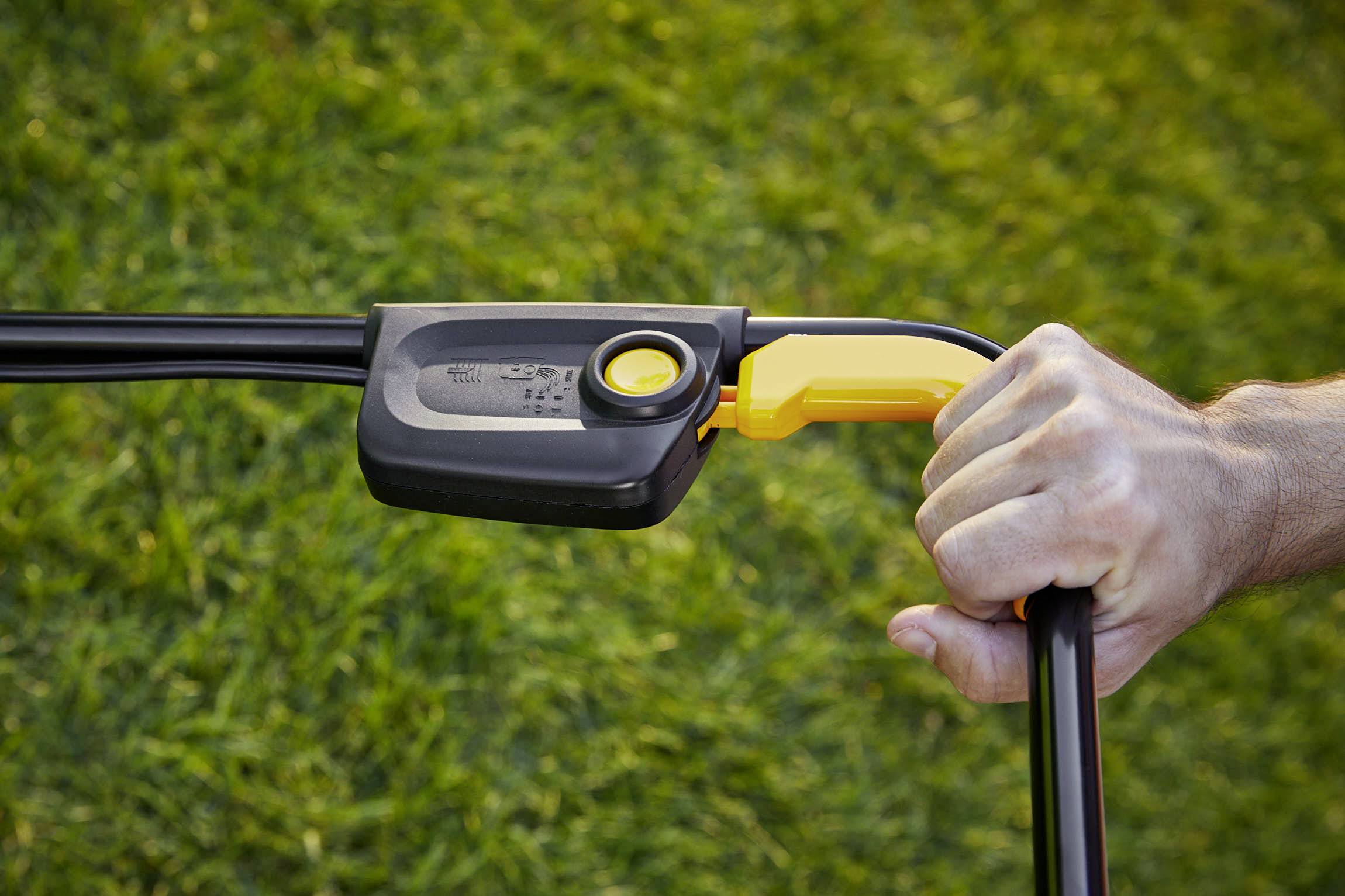 Close-up of a hand gripping a lawnmower handle. The background shows green grass.