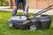 A person is operating an electric lawnmower on a green lawn. The mower has large wheels and a prominent yellow handle.