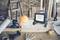 Workbench with building plans, hard hat, torch, drill and coffee mug. A brick wall and a ladder in the background.