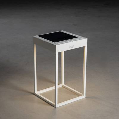 A white, square table with a solar panel on its top surface stands on a grey floor. Lighting on the interior side.