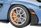 Close-up of a blue car showing the left front tyre with an orange brake behind a silver wheel rim.