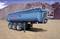 'Blue Schmitz Cargobull lorry trailer stands on a gravel surface in front of a large earth mound. The trailer has three axles.'