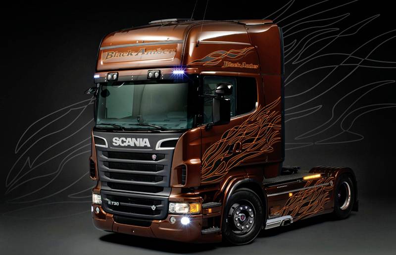 A brown lorry with flame decals stands in front of a dark background. 'Black Amber' is written on the windscreen.