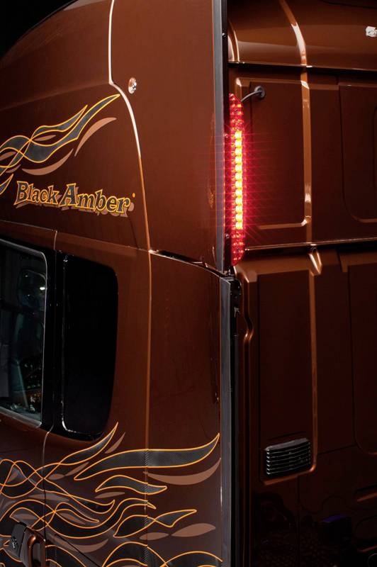 Rear view of a brown lorry with flame pattern and the inscription 'Black Amber'. A red tail light is illuminated.