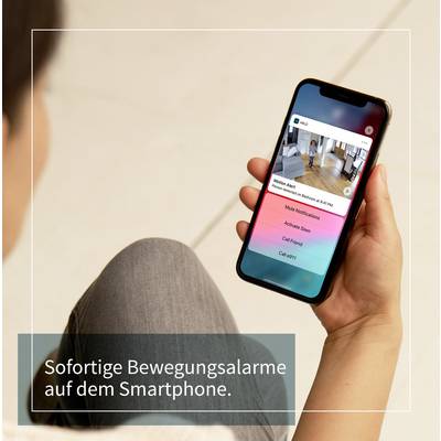 A person is holding a smartphone displaying a security camera app with a live feed. Text: 'Instant motion alerts on your smartphone.'