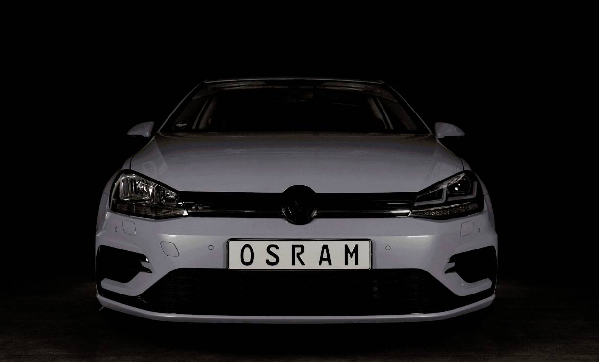 A car is positioned directly head-on against a black background. The number plate reads 'OSRAM'.