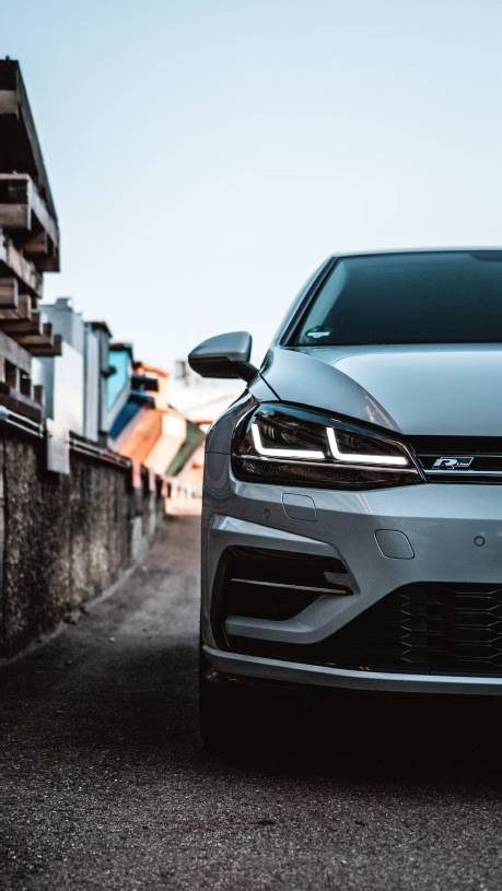 A grey car is parked on a street beside a building. The design is modern and buildings are visible in the background.