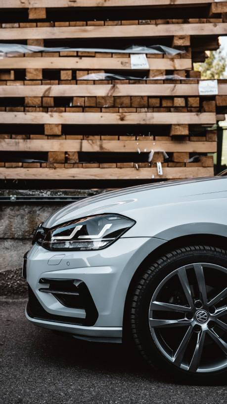 Front view of a silver car with a stack of wood in the background.