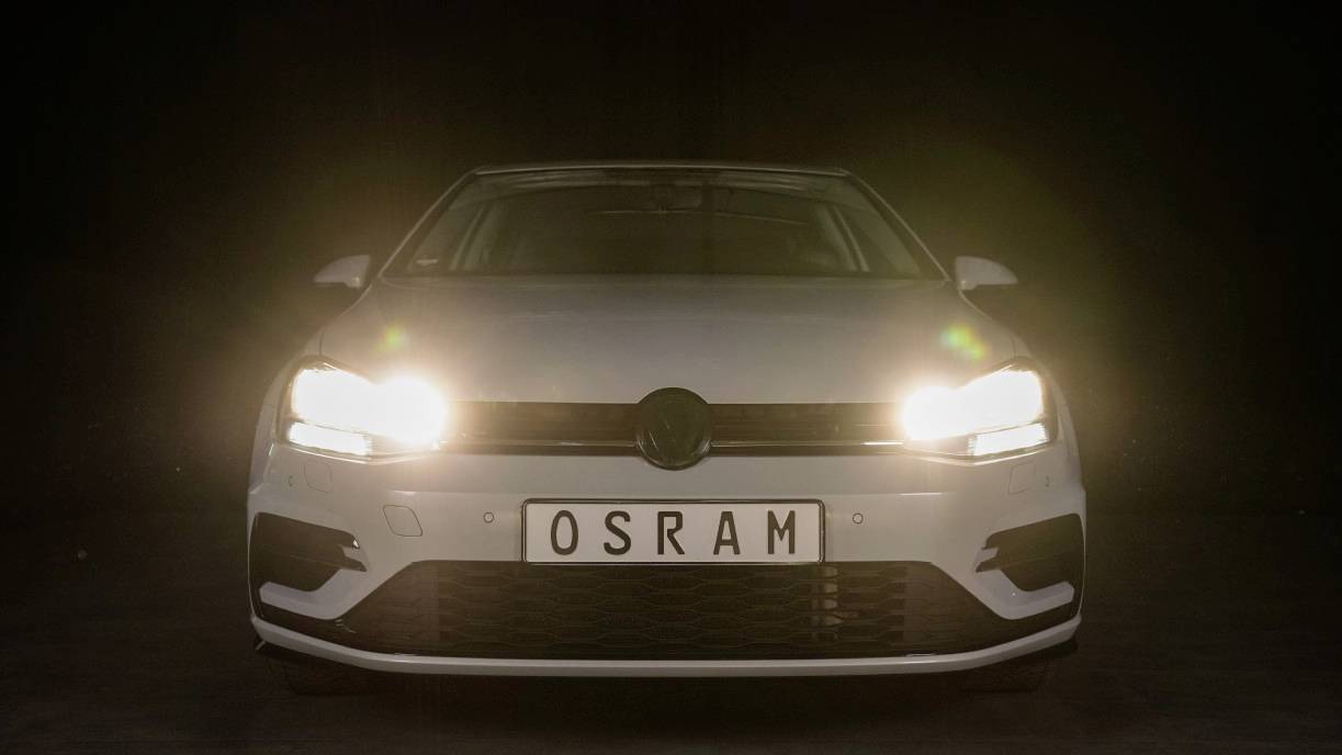 'A white car with headlights switched on in a dark room.'
