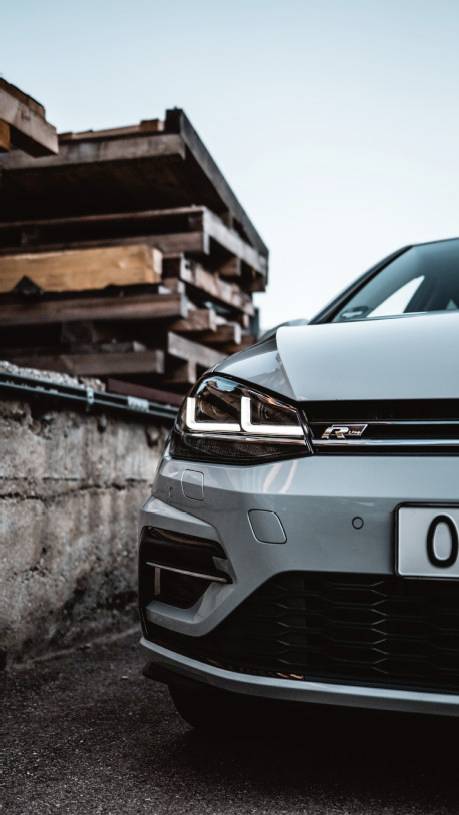 A grey car is partially visible in the foreground. Wooden boards are stacked in the background. The sky is cloudy.