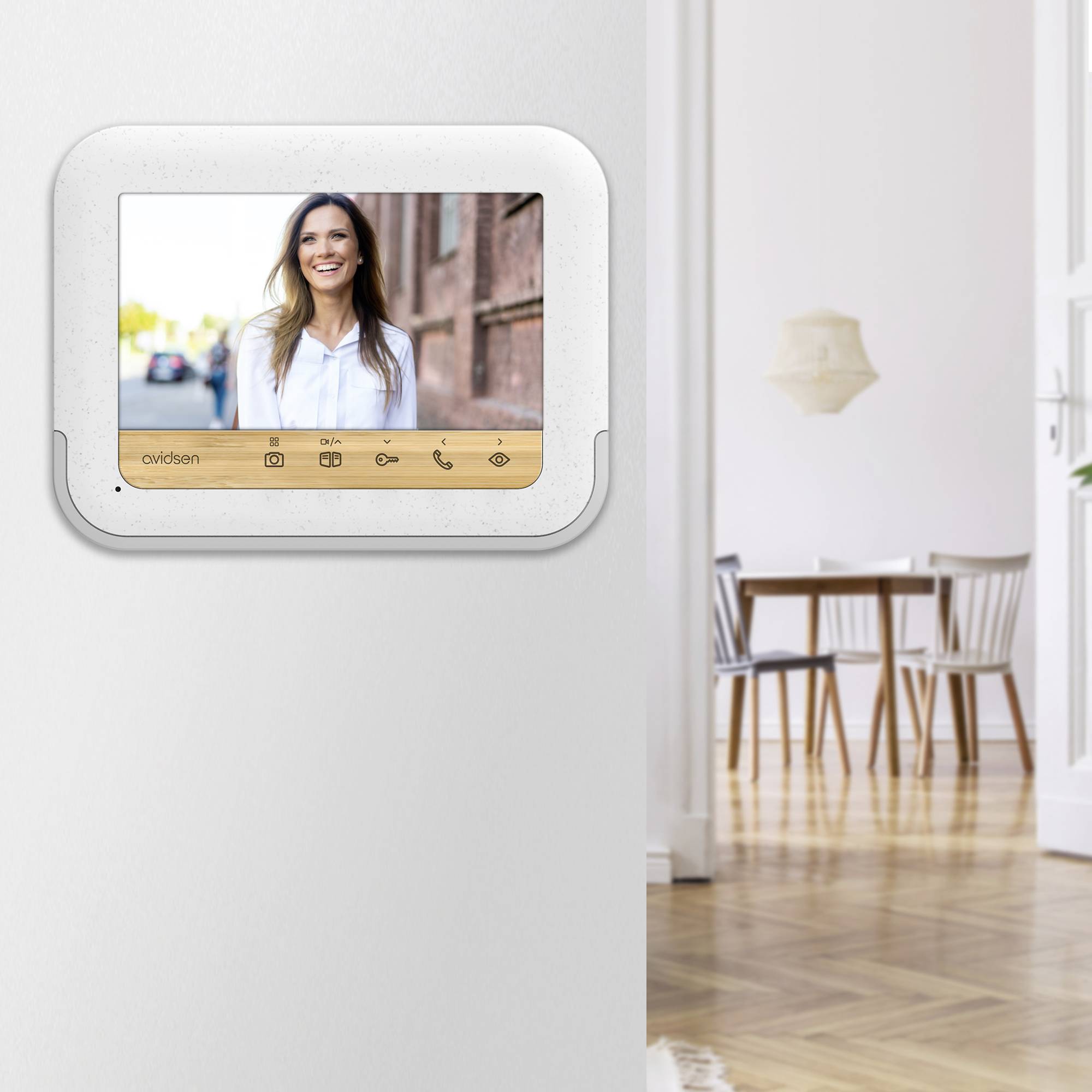 An internal monitor on the wall displays the image of a smiling woman. In the background, a dining room with a table and chairs can be seen.
