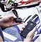 A person is holding a small electronic device and a smartphone with an app that is apparently connected to a motorbike.