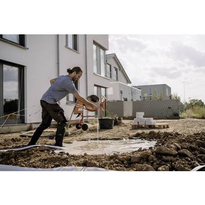 A person shoveling muddy water in a construction area beside white modern buildings under a cloudy sky.