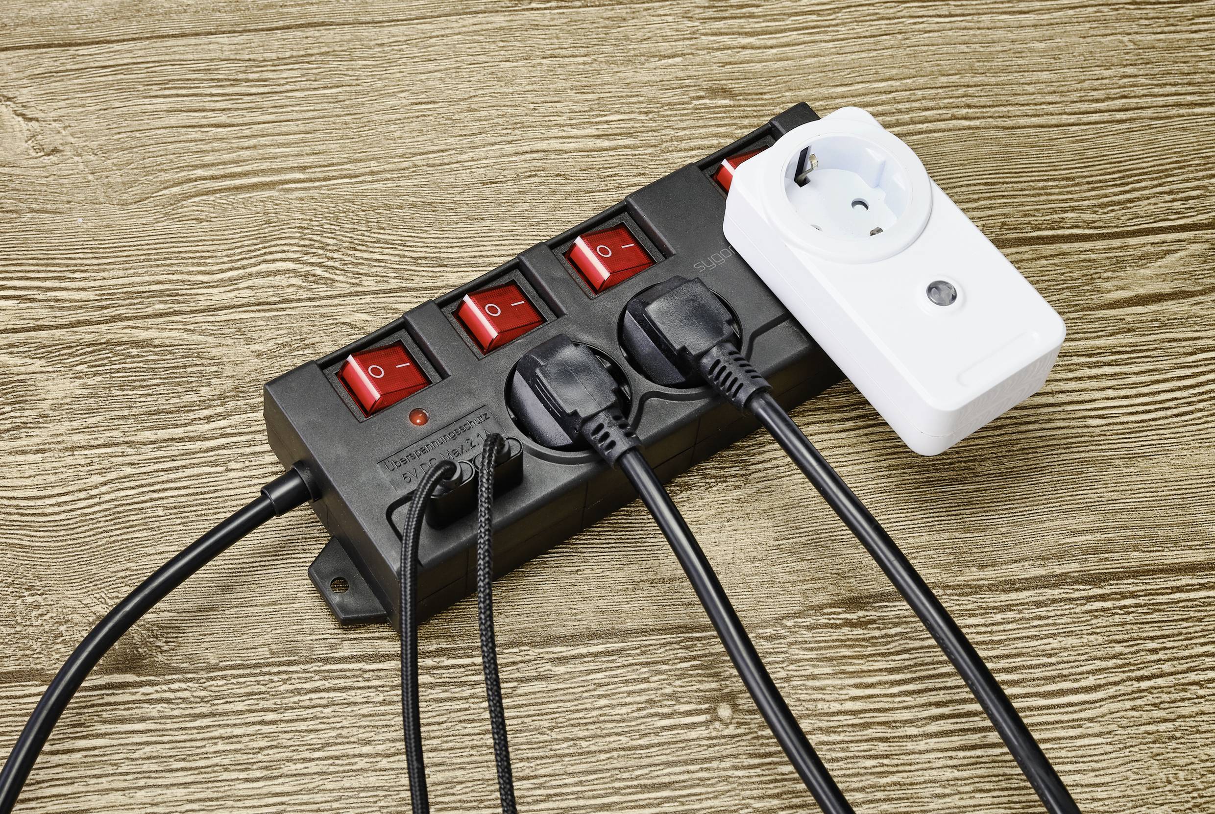 Several devices are connected to a black multi-socket extension lead with switches, and a white device is also plugged in.