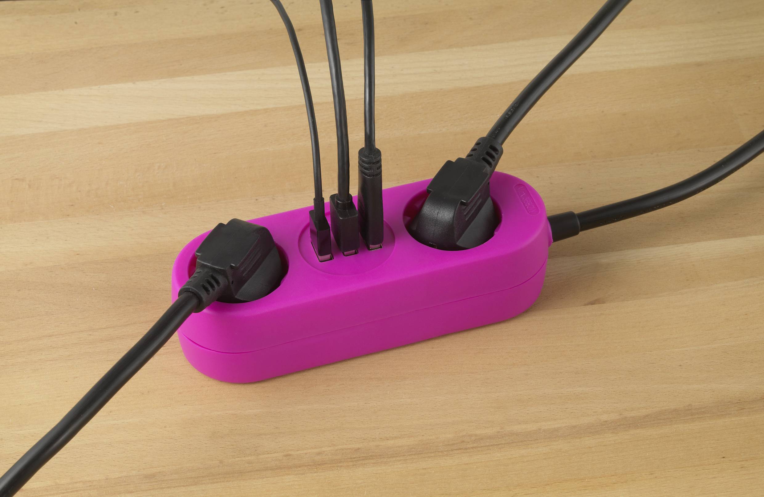 A pink multi-socket extension lead on a wooden table, with several black cables plugged in, enabling efficient power connections.
