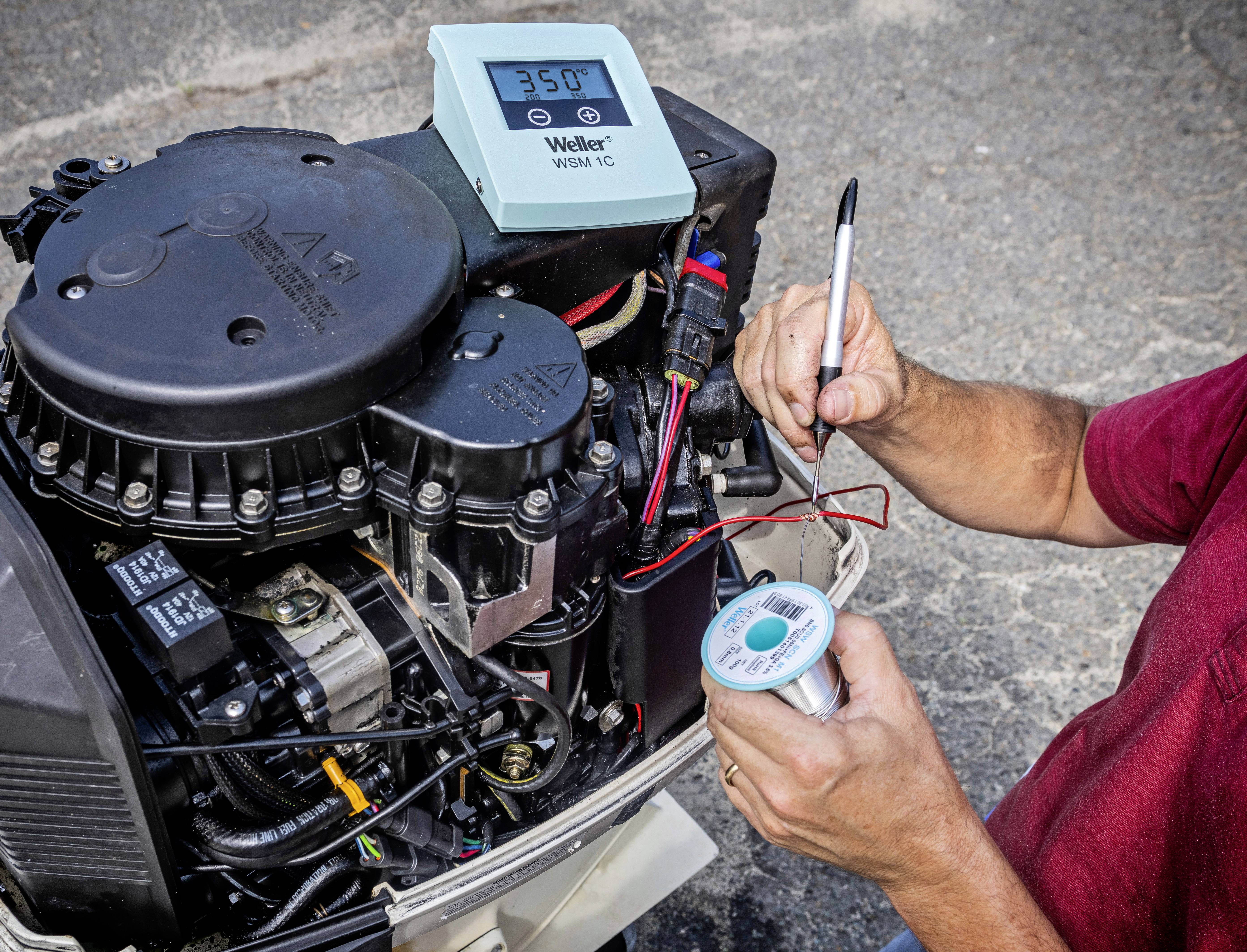 A person is soldering a motor with a soldering iron and solder. A temperature measuring device shows '350°'.