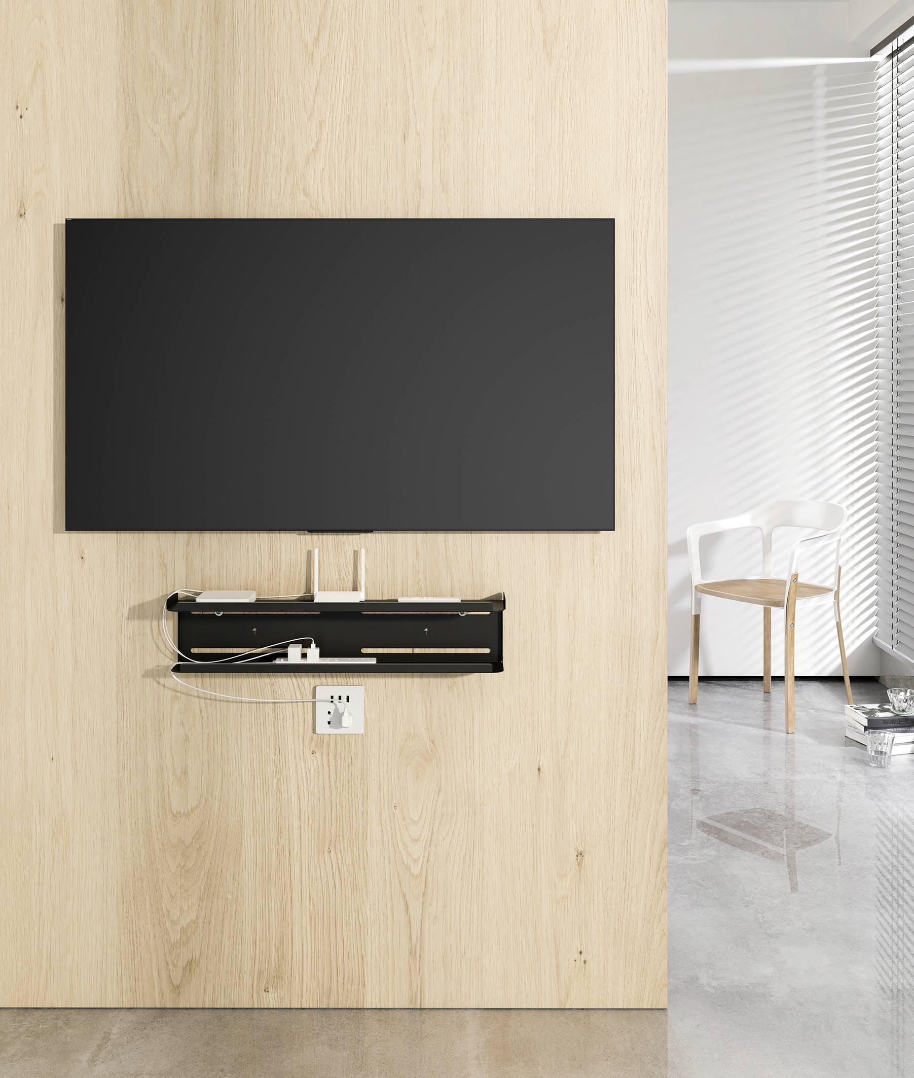 A television mounted on a wooden wall, with a shelf of electronic devices underneath. On the right, a white chair sits in front of a window.