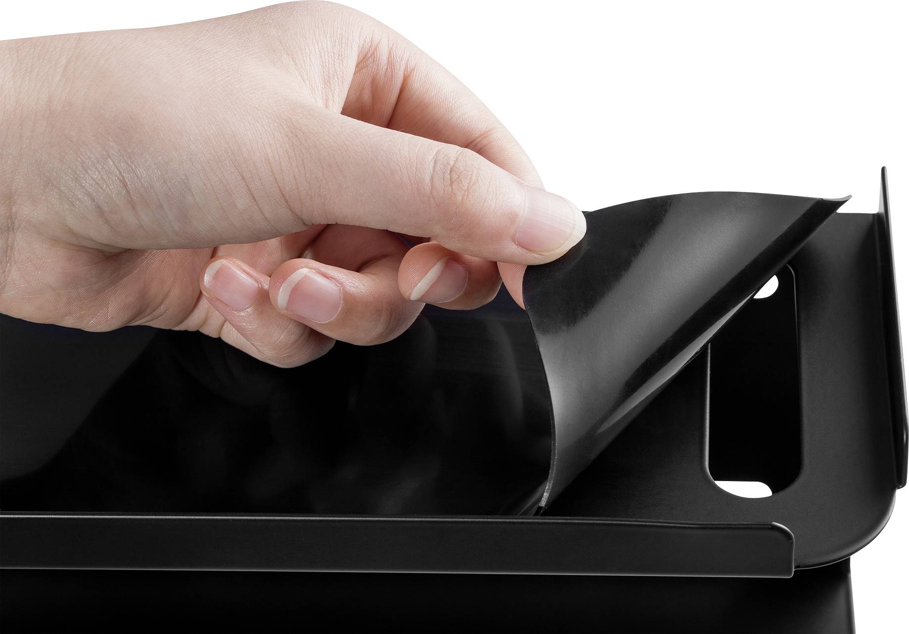 A hand carefully lifts a black, flexible film from a smooth, glossy surface. The background is neutral.