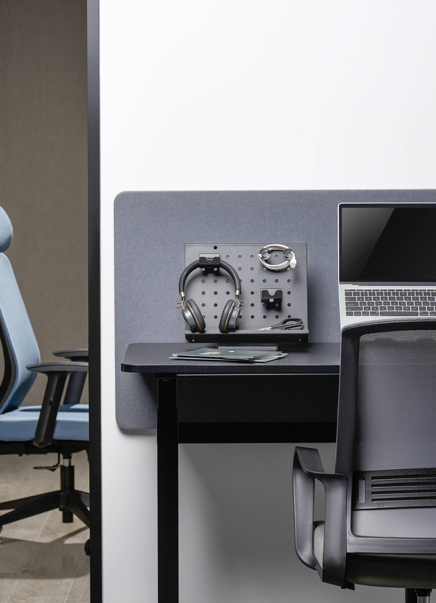 Desk with laptop, headphones and accessory board. In the background, a blue office chair. Modern office environment.