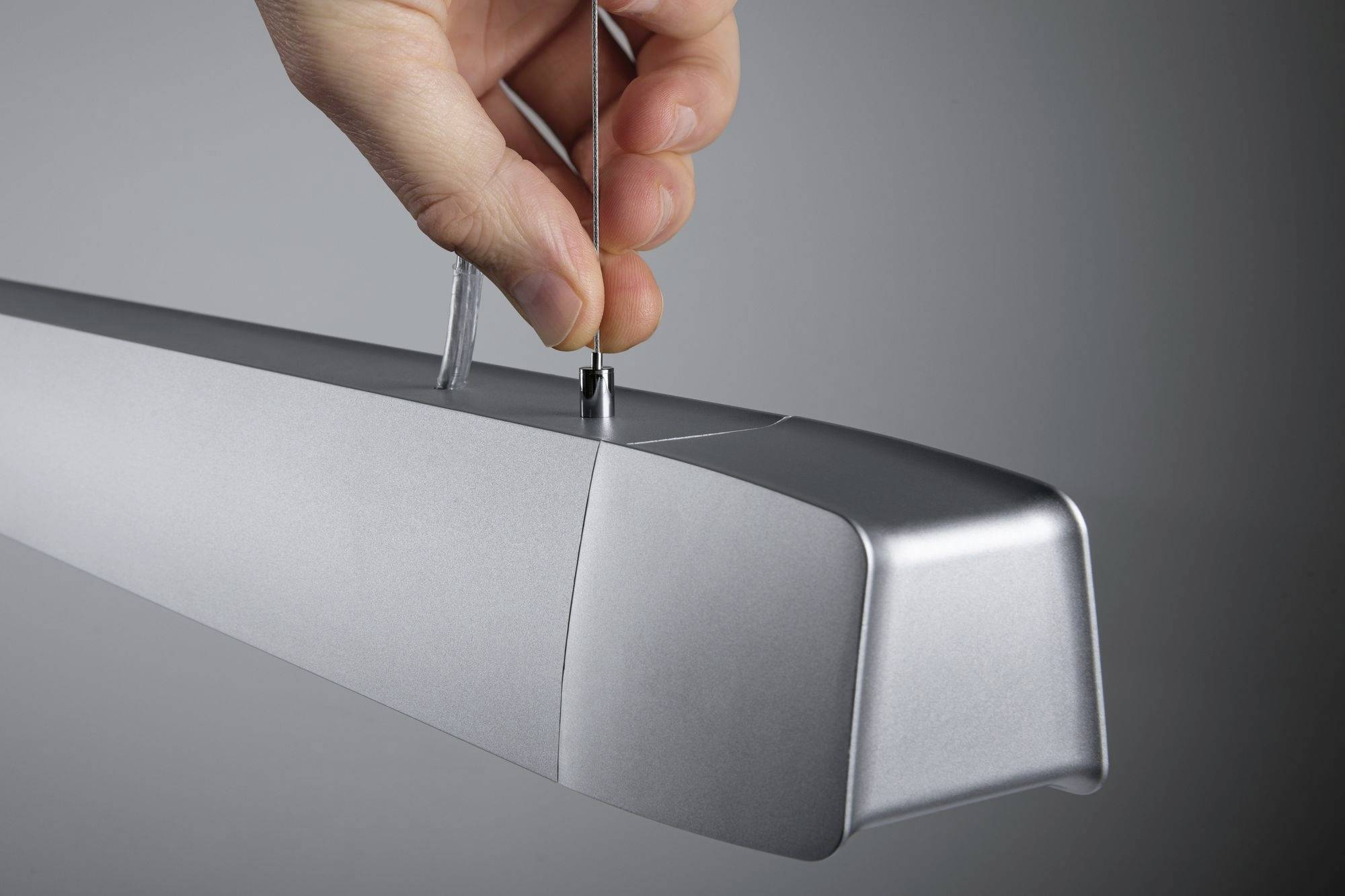 'A hand is securing a thin cable to a silver light fitting designed for ceiling mounting. The light fitting has a modern design.'